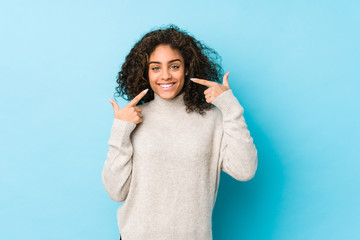 Young african american curly hair woman smiles, pointing fingers at mouth.