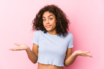 Young african american woman against a pink background doubting and shrugging shoulders in questioning gesture.
