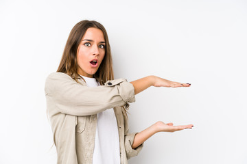 Young caucasian woman  isolated shocked and amazed holding a copy space between hands.