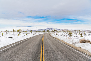 A highway curves toward distant mountains through a snow covered desert landscape