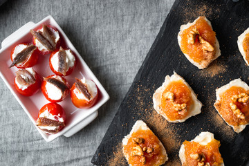 Still life of Goat roll cheese with jam and walnuts with cherry tomatoes stuffed with cheese and anchovies. Top view