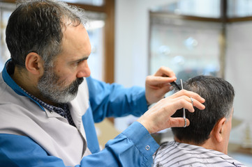 Barber trimming hair of old man at barber shop .