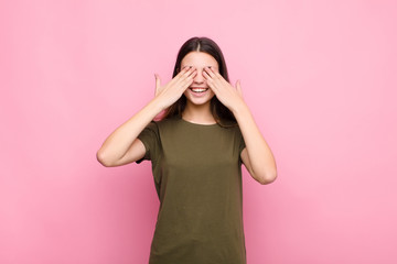 young pretty woman smiling and feeling happy, covering eyes with both hands and waiting for...