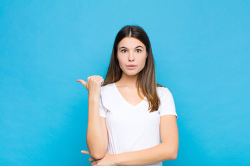 young pretty woman looking astonished in disbelief, pointing at object on the side and saying wow,...