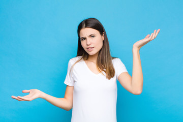 young pretty woman shrugging with a dumb, crazy, confused, puzzled expression, feeling annoyed and...