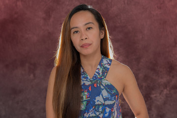 Fototapeta premium Young Filipina woman posing for studio headshots. Backlit on red and blue background