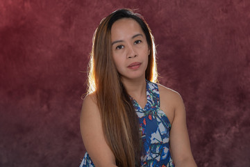 Young Filipina woman posing for studio headshots. Backlit on red and blue background