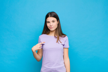 young pretty woman looking proud, confident and happy, smiling and pointing to self or making...