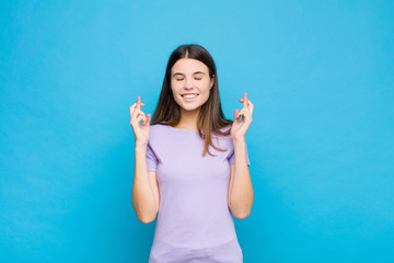 young pretty woman smiling and anxiously crossing both fingers, feeling worried and wishing or...