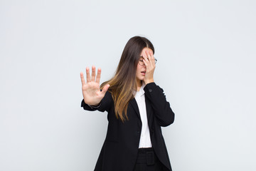 young businesswoman covering face with hand and putting other hand up front to stop camera,...