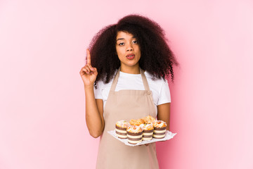 Young afro pastry maker woman holding a cupcakes isolatedYoung afro baker woman having some great idea, concept of creativity.