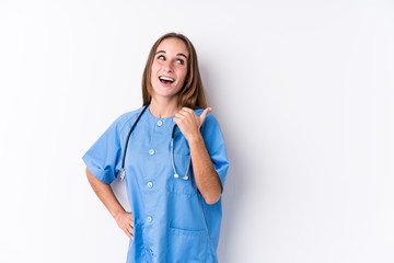 Young nurse woman isolated points with thumb finger away, laughing and carefree.