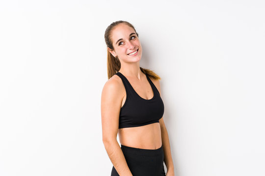 Young caucasian fitness woman posing in a white background looks aside smiling, cheerful and pleasant.
