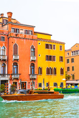 Fototapeta na wymiar Luxury wooden water taxi boat/ yacht sailing Grand Canal water/ waterway by colorful gothic Venetian architecture hotel, other buildings and striped mooring poles. Venice city, Italy in rainy November
