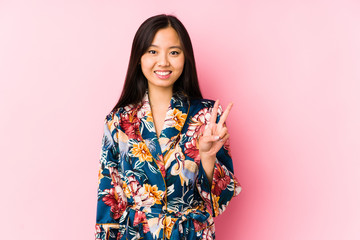 Young chinese woman wearing a kimono pajama isolated showing victory sign and smiling broadly.