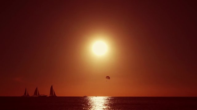 Parasailing flight against the backdrop of sunset. Dark silhouettes of sailing ships against a red sunset. Sea sunset, view from the beach. Yellow sun in the red sky.