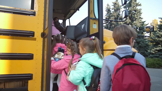 Rear view of diverse elementary age students pushing each other while getting on yellow school bus after lessons. Happy preadolescent schoolkids boarding school bus at the end of studies