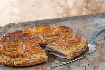 Epiphany Twelfth Night cake french galette des rois made of chocolate puff pastry, slice apart with the charm on wooden background
