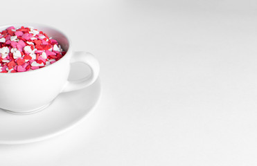 white cup of coffee on a white background filled with heart shaped confetti. selective focus. valentine day concept.