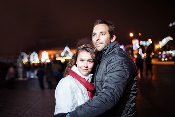 Fototapeta premium Loving couple on a date in a festive city with New Year's lights in the winter evening. Spouses in winter clothes Christmas.