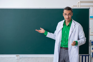 Young male chemist teacher in front of blackboard