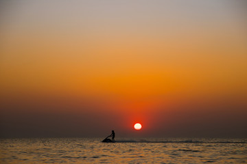 Silhouette of a man on a jet ski in the sea with sunset.