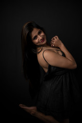 Obraz na płótnie Canvas Fashion portrait of an young and attractive Indian Bengali brunette girl with black western dress in front of a black studio background. Indian fashion portrait and lifestyle.