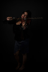 Fashion portrait of an young and attractive Indian Bengali brunette girl with black western dress is playing violin in front of a black studio background. Indian fashion portrait and lifestyle.