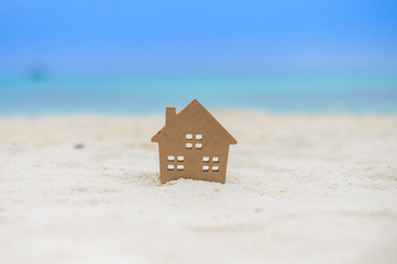 Fototapeta na wymiar Small home model on sand beach with blue sky background. Copy space of family lifestyle and business real estate concept.