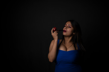 Close up fashion portrait of an young and attractive Indian Bengali brunette girl with blue western dress smoking pipe in front of a black studio background. Indian fashion portrait and lifestyle.