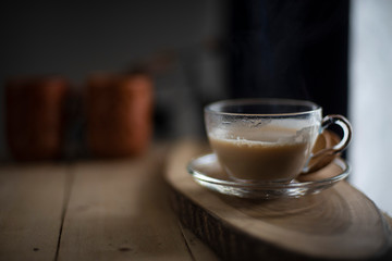 A transparent glass cup and soccer filled up with infused tea/coffee is kept in a wooden tray/table in black background in the winter morning. Indian beverages and food photography.