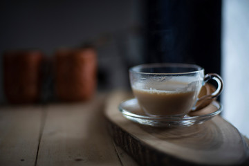A transparent glass cup and soccer filled up with infused tea/coffee is kept in a wooden tray/table in black background in the winter morning. Indian beverages and food photography.