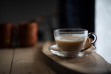 A transparent glass cup and soccer filled up with infused tea/coffee is kept in a wooden tray/table in black background in the winter morning. Indian beverages and food photography.