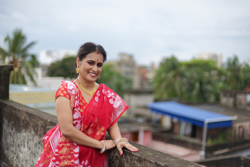 Portrait of a beautiful smiling brunette Indian Bengali woman in traditional red sari standing on...