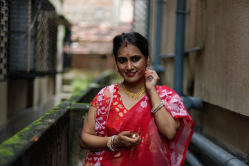Portrait of a beautiful smiling brunette Indian Bengali woman in traditional red sari standing in a...