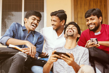 Group of happy young college students by looking at mobile phone laughing loudly at university...