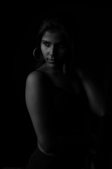 Fototapeta na wymiar Monochrome fashion portrait of an Indian brunette Bengali dark skinned woman with black lingerie standing in black studio copy space background. Indian fashion photography and lifestyle.