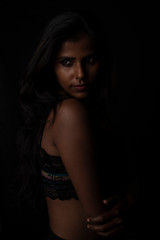 Obraz na płótnie Canvas Fashion portrait of an Indian brunette Bengali dark skinned woman with black lingerie standing in black studio copy space background. Indian fashion photography and lifestyle.