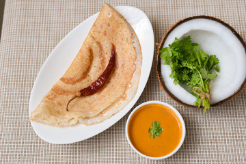 Dosa and Coconut chutney with fresh raw coconut cut in half with coriander leaf on white background in Kerala Tamil Nadu South India. Top view of Indian veg breakfast food.