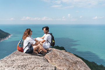 Fototapeta na wymiar Happy beautiful young couple of travelers man and woman on top of a mountain with ocean view. Romantic travels, honeymoon,