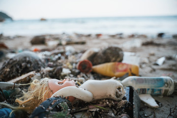 The concept of pollution of nature and the oceans, plastic trash on the beach, a broken baby doll lies on the sand