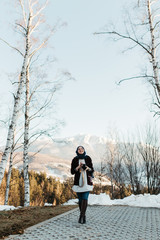 portrait of young European Muslim women with hijab standing on the edge of the mountain. She is holding hat in one hand and waving with the other. She is also holding camera and taking pictures.