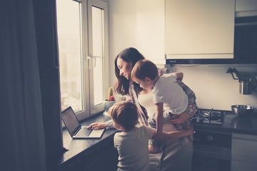 Busy mom with two children works on laptop kitchen