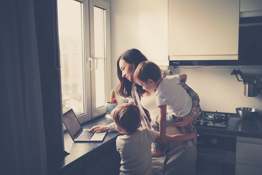 Busy Mom With Two Children Works On Laptop Kitchen