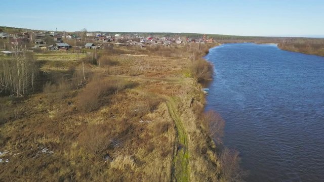 Natural landscape with wide river and the field with yellow grass and snow in early spring. Clip. Aerial of small village on blue cloudy sky background.
