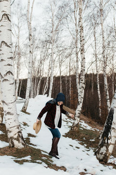 Young woman walking in snow outdoors in forest. She is relaxing on an outdoor walk activity in snowy forest landscape wearing brown boots, scarf and hat. 