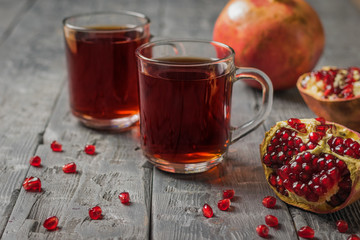Glass mugs of pomegranate juice and ripe pomegranate fruit on a rustic table.