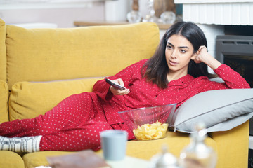 Persian woman at home watching TV and using remote control