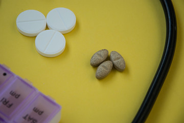Bunch of pills and capsules, box for storage of drugs and medical stethoscope and blood pressure meter on yellow background, healthcare concept