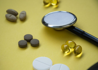 Bunch of pills and capsules and medical stethoscope and blood pressure meter on yellow background, healthcare concept
